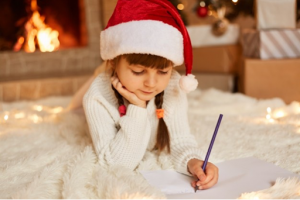 little girl writing a letter to santa in a santa hat near the fireplace in a luxury home in portofino alabang | Luxury homes by Brittany Corporation