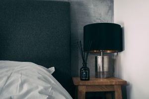 A photo of a diffuser placed on top of a brown wooden bedside table with a lamp on the side | luxury homes by brittany corporation