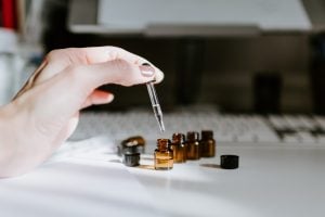 A photo of essential oil bottles on a table, featuring a hand holding a glass dropper | luxury homes by brittany corporation