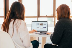 A photo of two women talking while facing a laptop. | luxury homes by brittany corporation