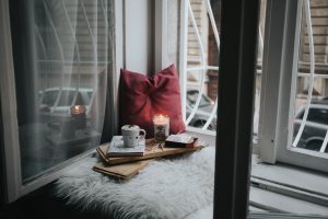 Photo of a lighted candle, pillow, and hot choc beside the window. | luxury homes by brittany corporation