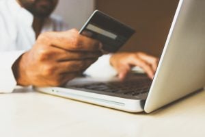 Photo of a person’s hand holding a card in front of a laptop | luxury homes by brittany corporation