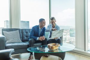 Two men in suits sitting on a sofa and smiling | luxury homes by brittany corporation