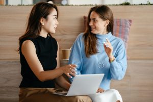 Two women talking with an open laptop.