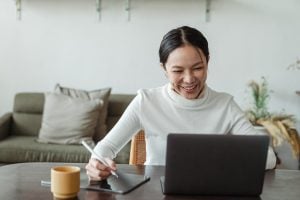 Woman smiling while talking, watching from laptop and taking notes. | Luxury homes by brittany corporation