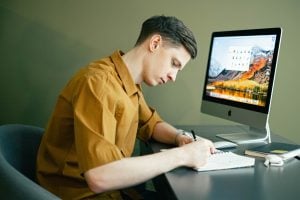 Young man taking notes on a pad in front of his computer. | luxury homes by brittany corporation