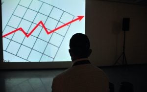 Image of a man standing in front of a projector showing a rising chart. | luxury homes by brittany corporation