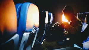 man inside an airplane looking in his bag against the sunlight | luxury homes by brittany corporation
