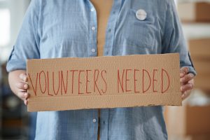 woman holding a volunteers needed poster | luxury homes by brittany corporation
