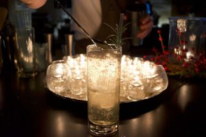 clear liquid inside a glass surrounded by empty glasses with a rosemary as garnish | luxury homes by brittany corporation