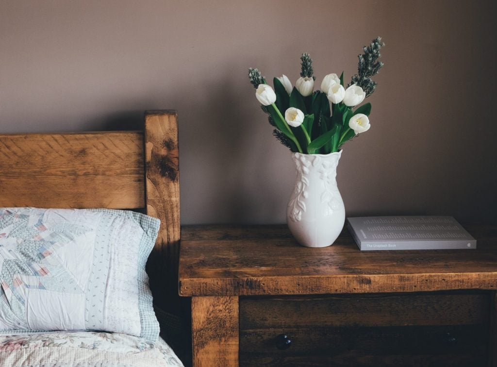 Adding Floral Accents To Real Estate Decor Photo of white tulips arranged inside a white porcelain vase that is placed above a wooden bedside table