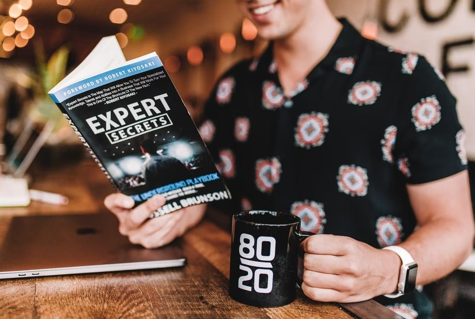 smiling man reading book while holding mug expertise