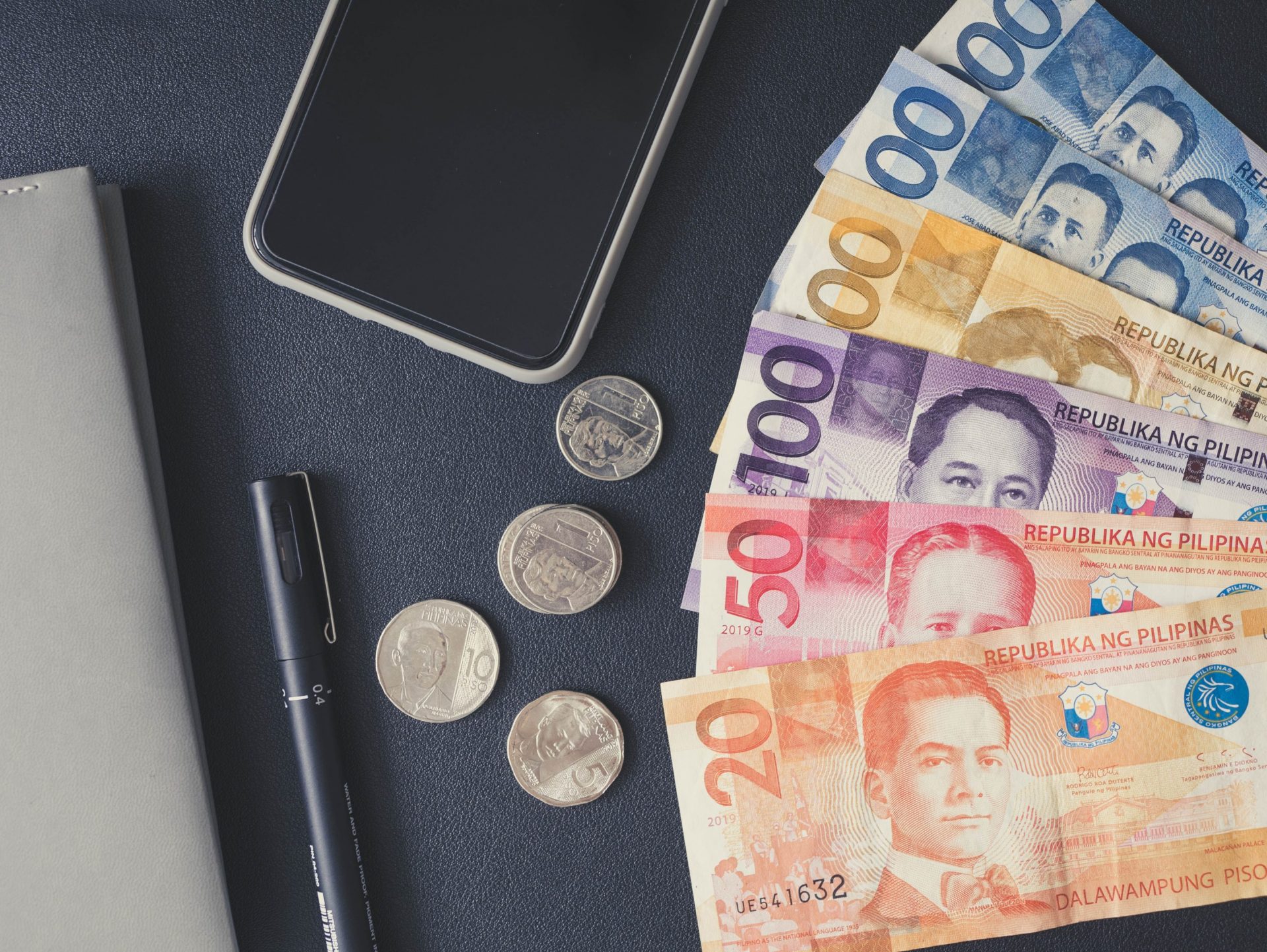 Flatlay photo of Philippine currency on the table beside a ballpen and phone