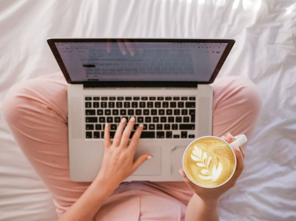 Photo of a person holding a cup of coffee while using laptop