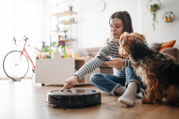 Woman using smart phone to control and turn on robotic vacuum cleaner.