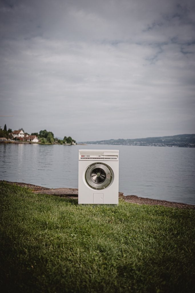 white front load washing machine on green grass field near body of water during daytime