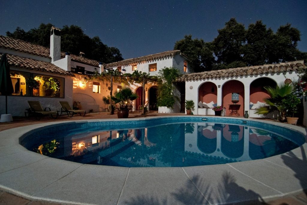 A circular swimming pool in front of a white house with a cobbled roof