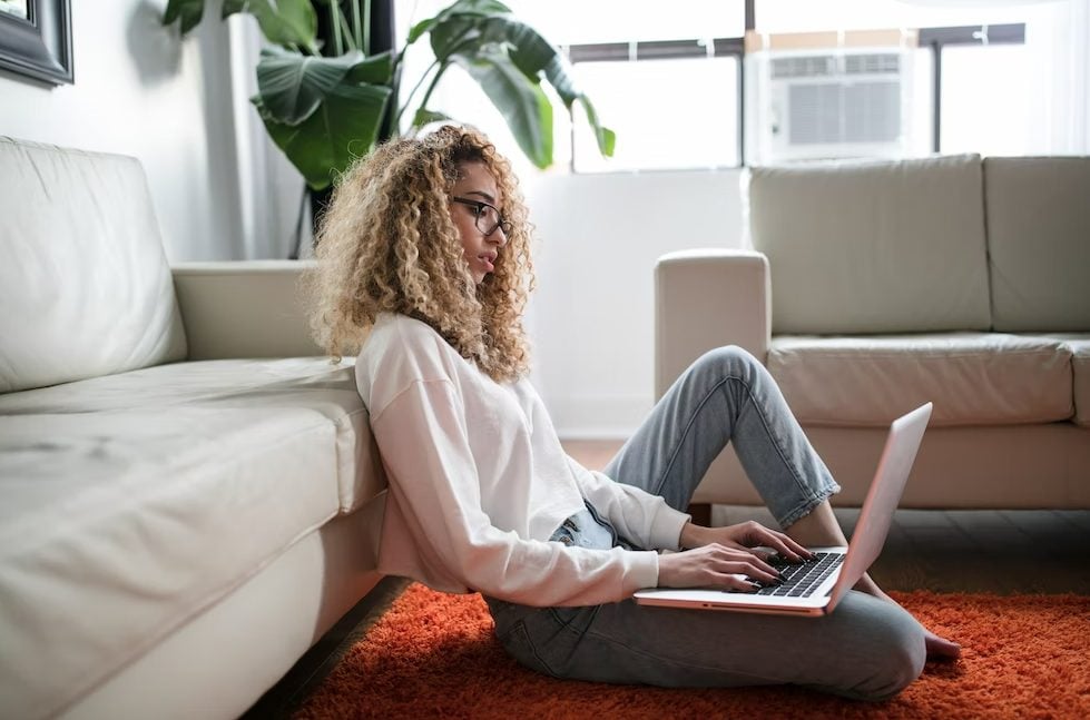 woman sitting on floor and leaning on couch using laptop