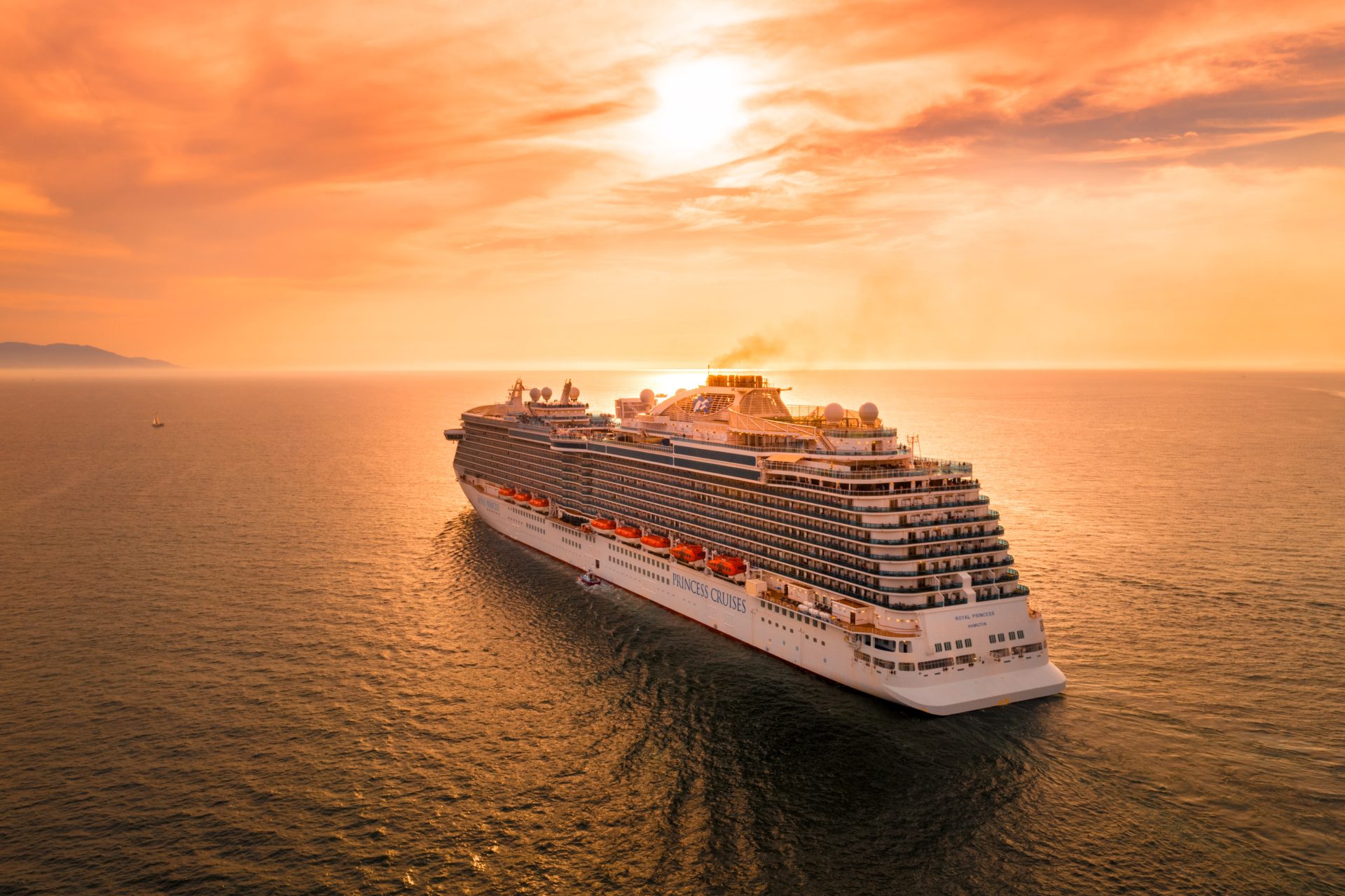 A sailing cruise ship on a sunset backdrop.