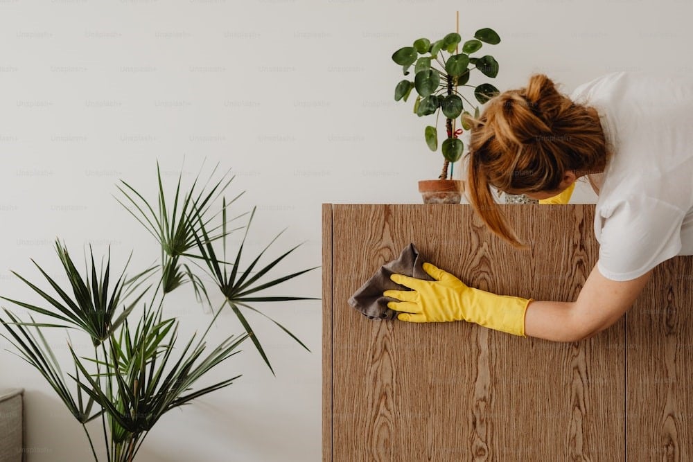 Photo of a woman in a white shirt and yellow gloves cleaning a wooden cabinet
